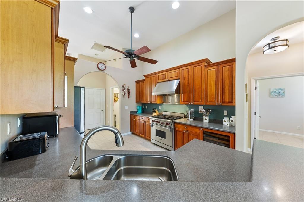 Kitchen featuring arched walkways, appliances with stainless steel finishes, beverage cooler, under cabinet range hood, and ceiling fan