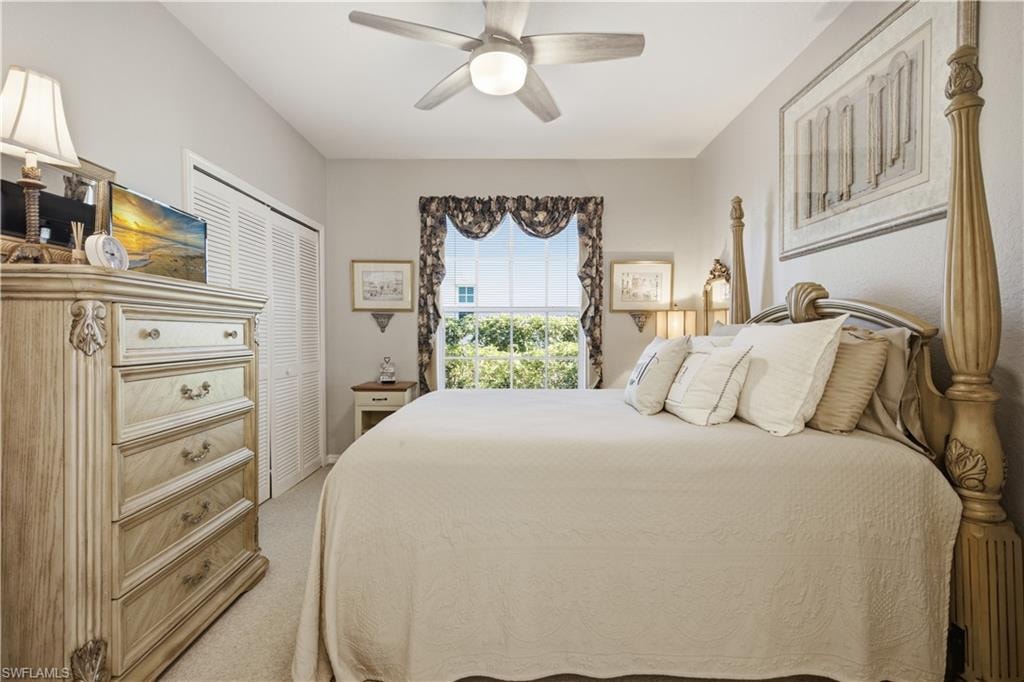 Carpeted bedroom featuring a large window with patterned valance, louvered bi-fold closet doors, a ceiling fan with integrated lighting, and neutral wall tones