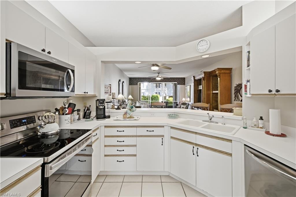 White kitchen featuring a double basin sink, stainless steel appliances, white cabinetry with dark hardware, and light-toned countertops