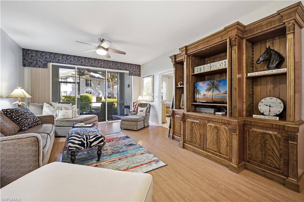 Living area featuring a floor-to-ceiling custom wood built-in entertainment center with integrated shelving, wood-finish flooring, and a ceiling fan with integrated lighting