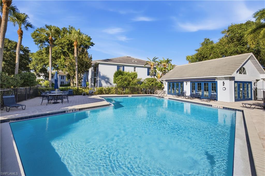 Expansive outdoor swimming pool with a surrounding paver deck and a pool house featuring multiple sets of blue French doors