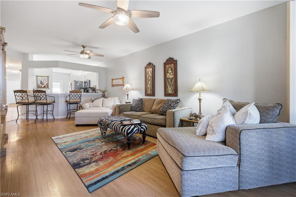 Spacious interior featuring wood-finish flooring, two ceiling fans with integrated lighting, and a kitchen pass-through with a breakfast bar