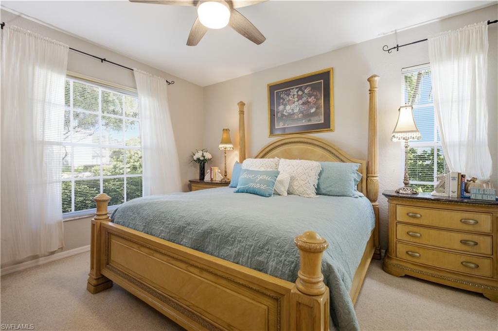 Spacious room featuring neutral carpeting, two large windows with blinds and sheer curtains, a ceiling fan with integrated lighting, and light-toned wall paint