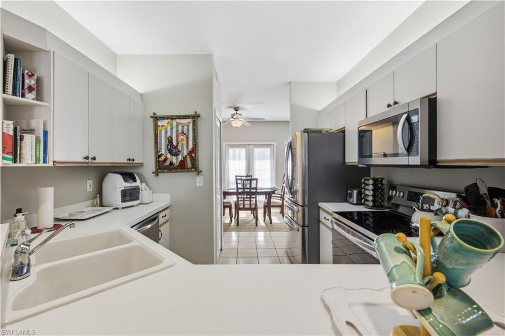 Kitchen featuring white cabinetry, light-colored countertops, a stainless steel microwave, a black electric range, and a double-basin sink