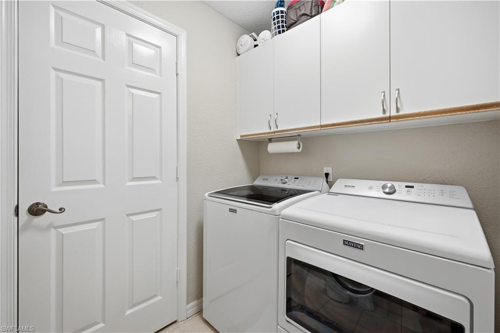 Dedicated laundry area featuring white upper cabinetry with brushed nickel hardware, a wood-finish shelf, and light-toned wall paint