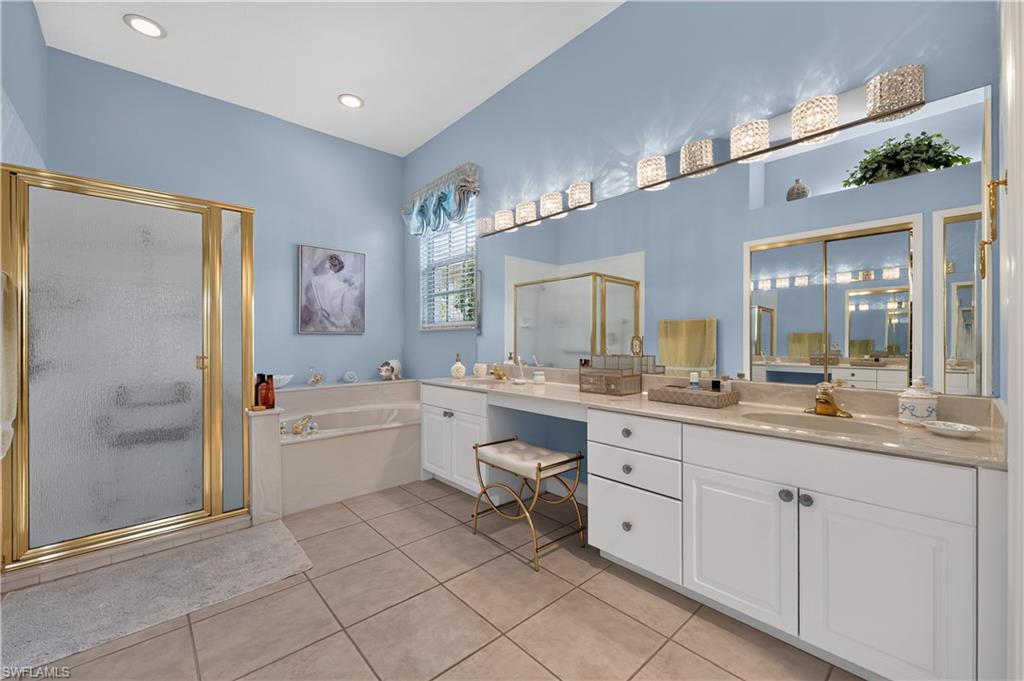 Spacious bathroom featuring a glass-enclosed shower with gold-tone framing, a built-in soaking tub, and a dual vanity with ample countertop space