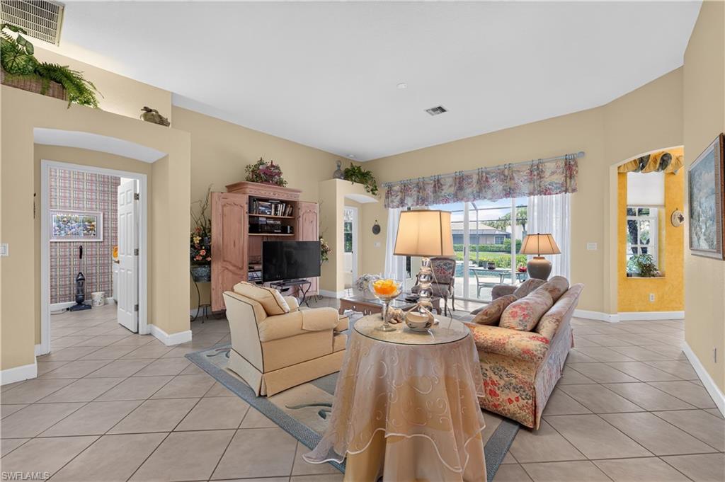 Spacious living area featuring tile flooring, vaulted ceilings, an arched doorway, and large windows overlooking an outdoor pool area