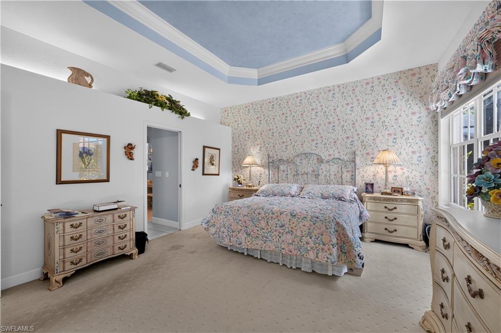 Room featuring a tray ceiling with a blue finish, patterned wallpaper, and light-colored carpeting