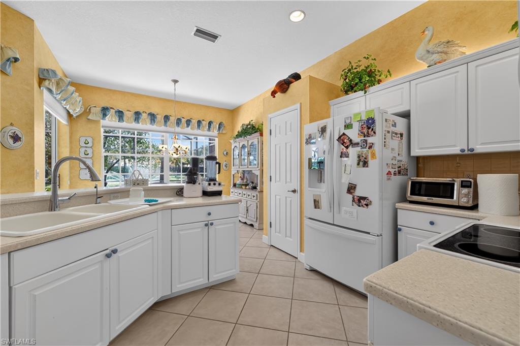 Kitchen featuring white cabinetry, light-toned countertops, a dual basin sink with a high-arc faucet, and tiled flooring