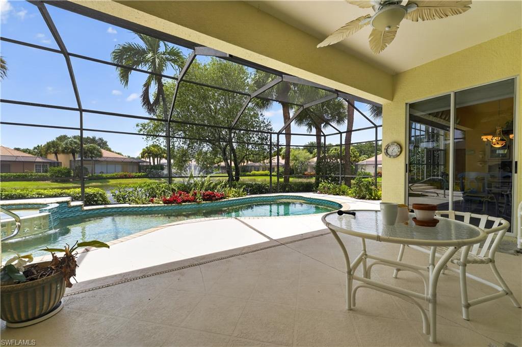 Screened lanai featuring a curved swimming pool with integrated spa and waterfall, a textured concrete deck, and a ceiling fan