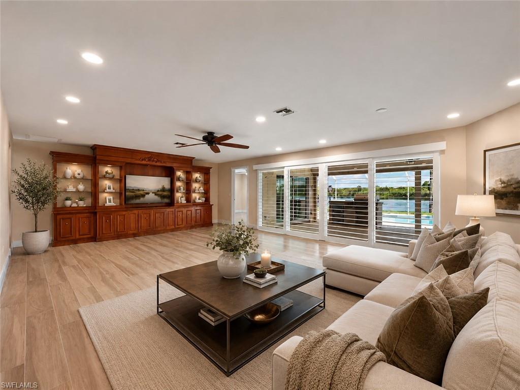 Spacious living area featuring expansive sliding glass doors, built-in entertainment center with display shelving and accent lighting, wood-finish flooring, and recessed lighting