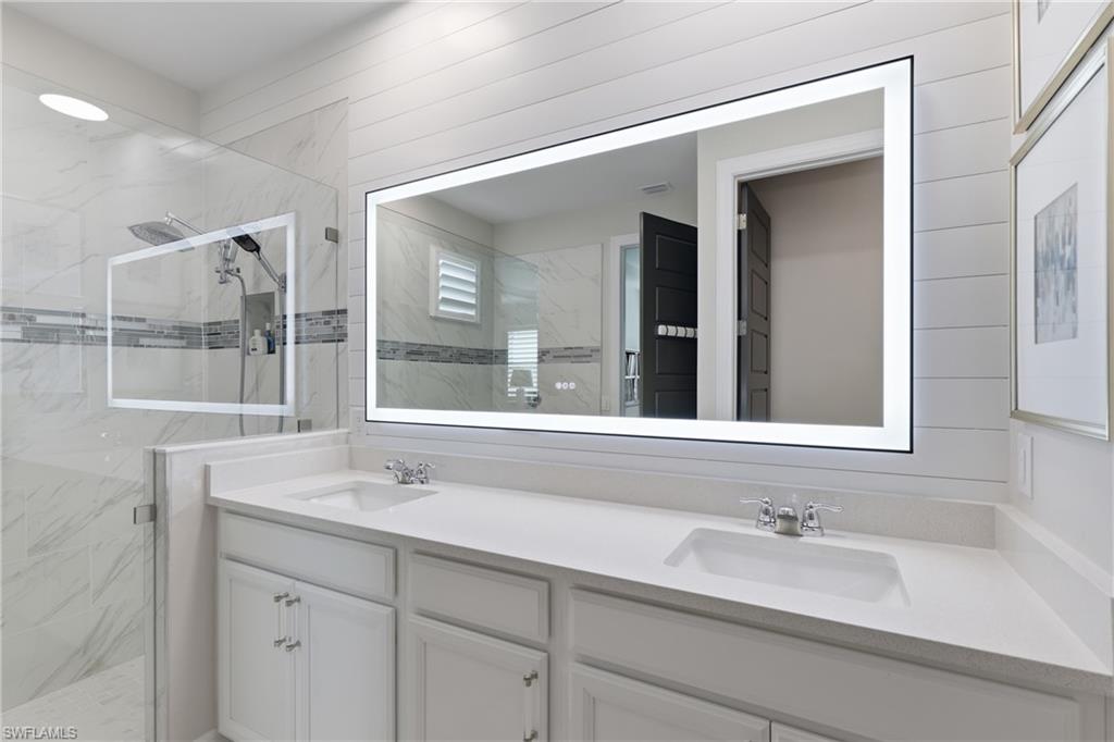 Spa-inspired owners bath with a dual vanity and frameless glass shower and elegant lighted mirror