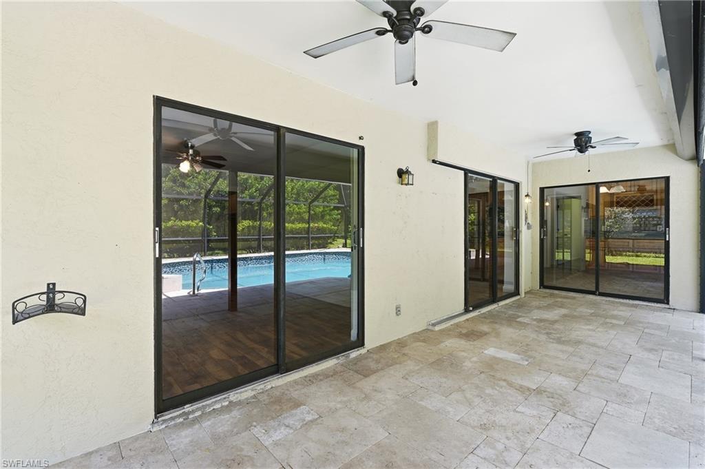 Tiled patio featuring multiple sliding glass doors, two ceiling fans, and an exterior wall lantern