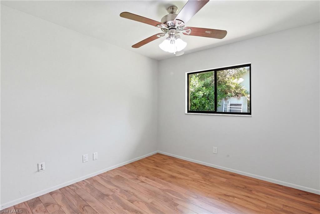 Room featuring wood-finish flooring, a ceiling fan with integrated lighting, and a window with a dark frame