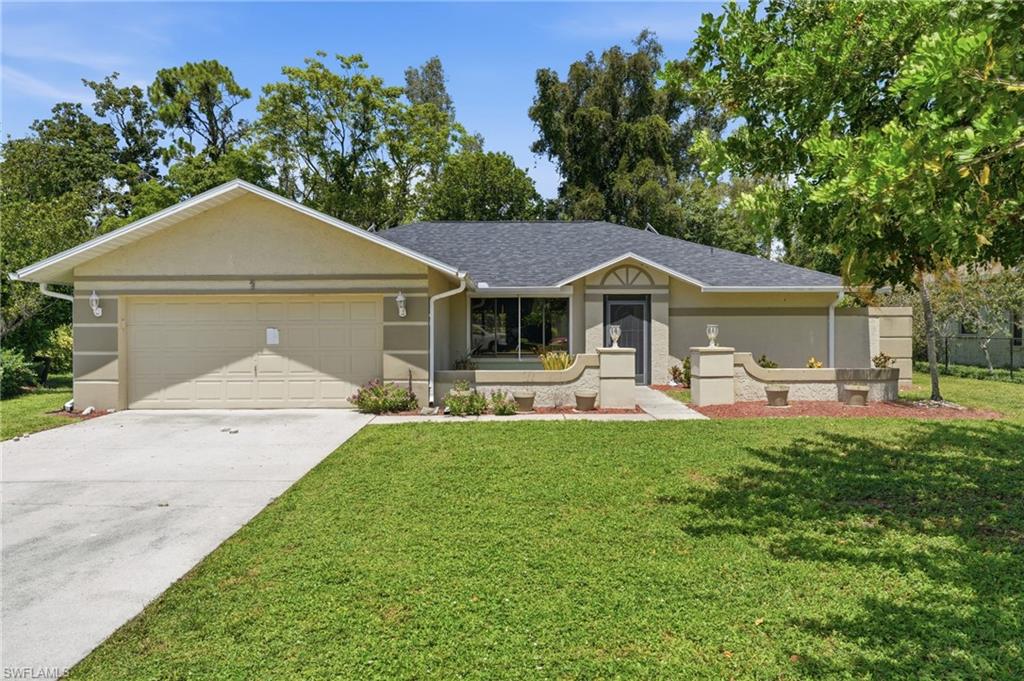 Traditional-style residence featuring a stucco exterior, an attached garage, a dark shingled roof, a paved driveway, and established landscaping
