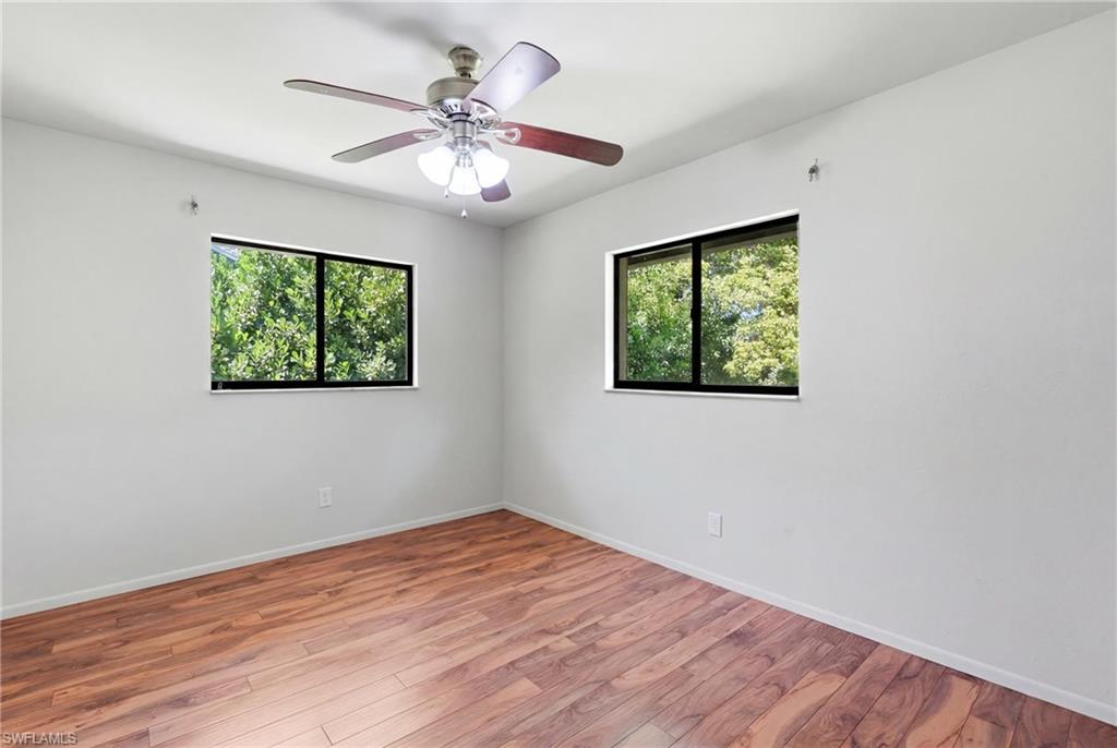 Room featuring wood-finish flooring, two windows with black frames, and a ceiling fan with integrated lighting
