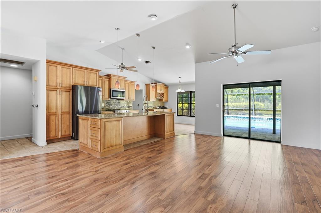 Open-concept living space with vaulted ceilings, wood-finish flooring, a kitchen island, pendant lighting, and sliding glass doors leading to a screened pool area