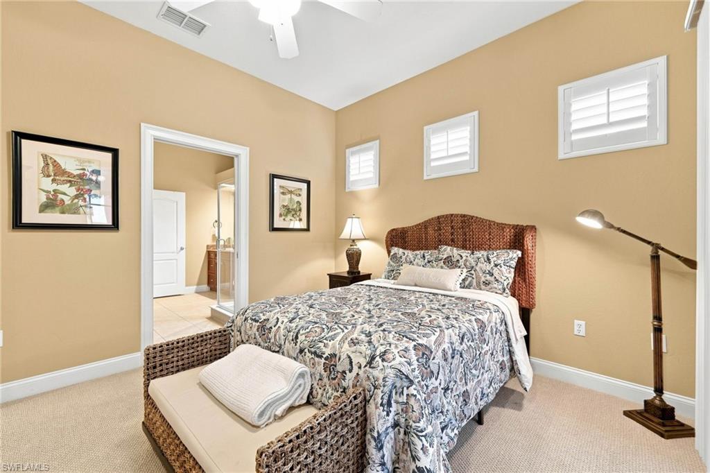 Spacious primary bedroom showcasing warm neutral walls, abundant natural light from multiple transom windows, a decorative upholstered bed frame, ceiling fan, hardwood flooring, and woven storage benches
