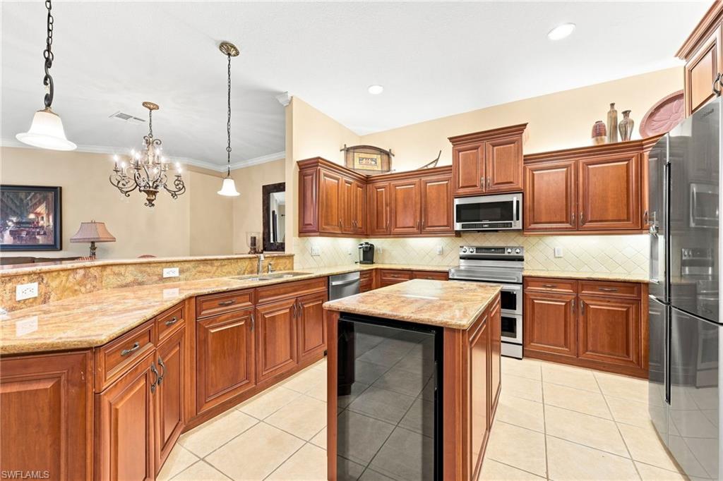 Spacious kitchen featuring rich wood cabinetry, granite countertops, a large center island with black base, stainless steel appliances including a gas range and refrigerator, pendant lighting, and ceramic tile flooring