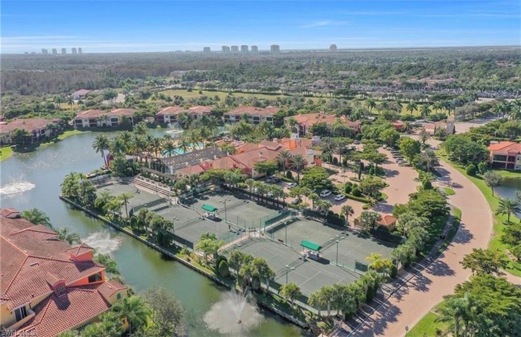 Aerial perspective showcasing residential buildings with terracotta-style roofing, multiple tennis courts, and a central clubhouse with an outdoor pool