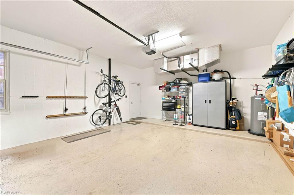 Spacious garage featuring epoxy-coated concrete flooring, abundant natural lighting from overhead fixtures, wall-mounted bike storage system, built-in cabinetry and shelving units, and ample room for vehicles and equipment storage
