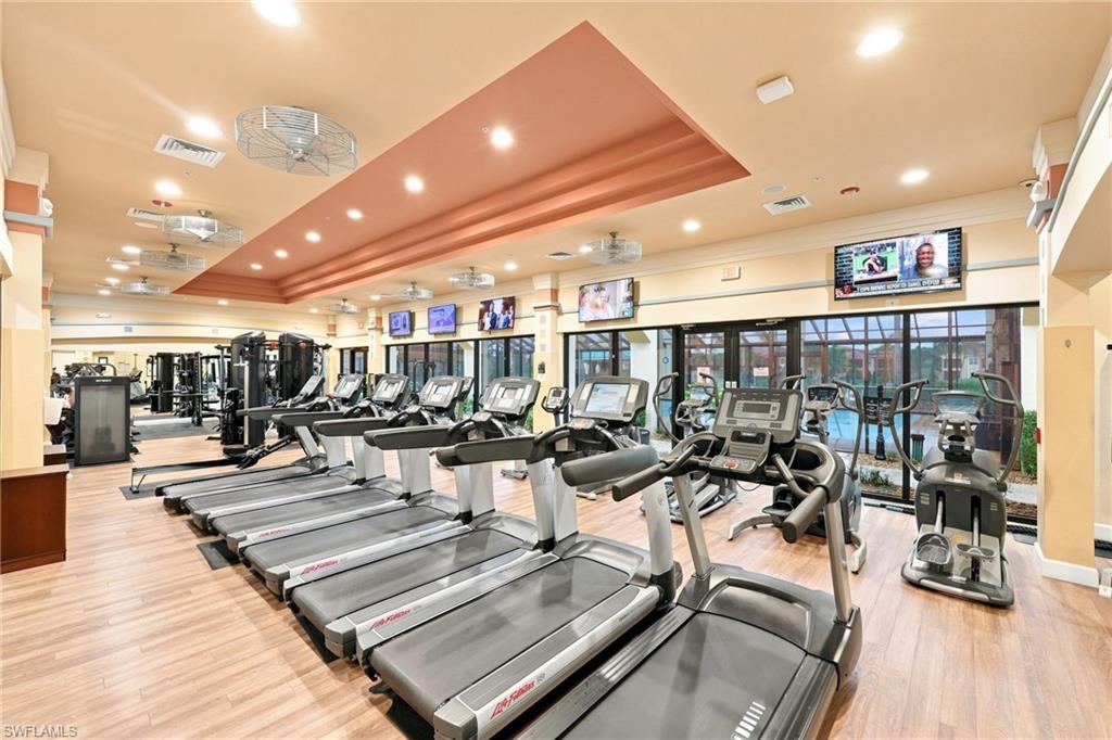 State-of-the-art fitness facility featuring multiple treadmills with individual entertainment displays, comprehensive strength training equipment, wood-finish flooring throughout, recessed and pendant lighting, and expansive windows providing natural light and outdoor visibility