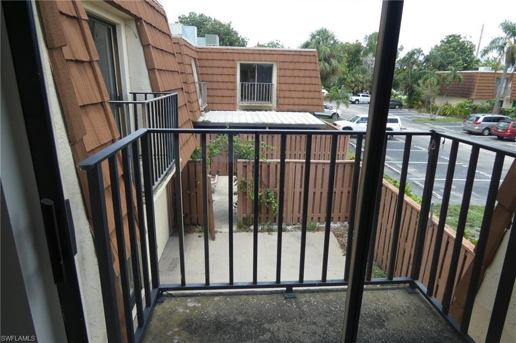Private balcony with dark metal railings overlooking a fenced courtyard and parking area