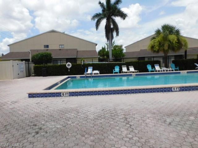 Outdoor swimming pool featuring a patterned paver deck, blue and white mosaic tile border, and a black wrought iron fence