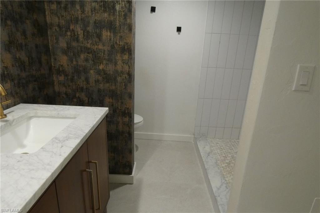 Modern bathroom featuring a vanity with a white countertop and gold-finish faucet, a decorative accent wall, a shower with vertical white subway tile, and a pebble-stone shower floor