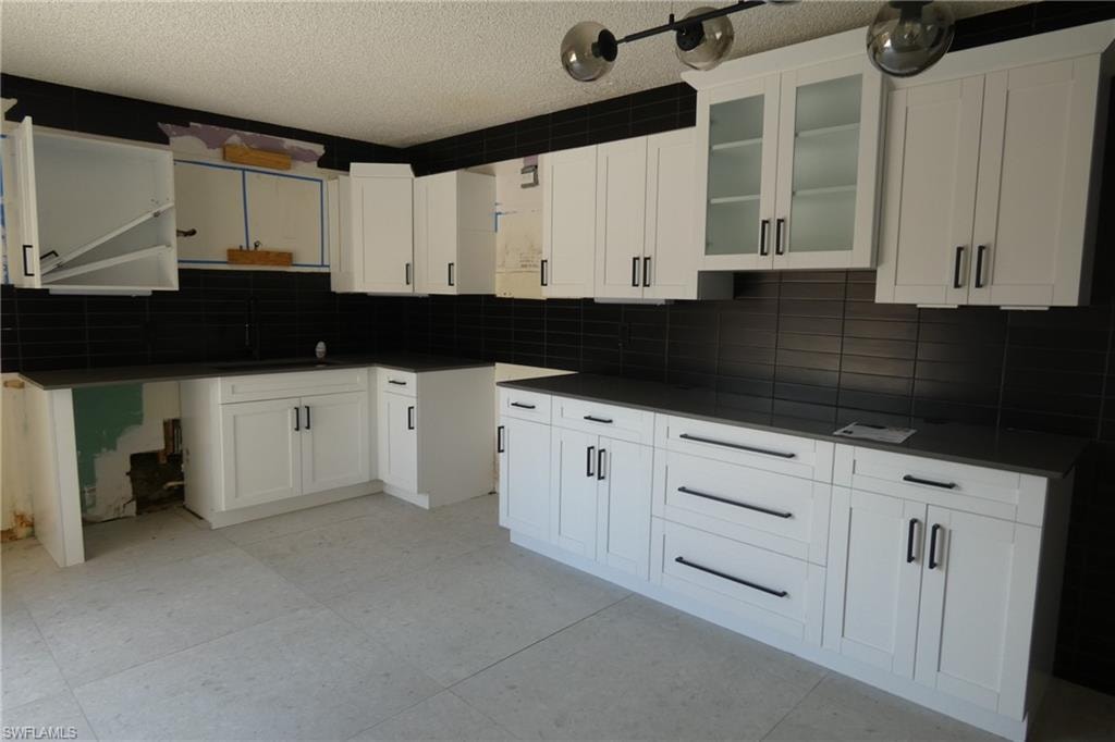 Contemporary kitchen featuring white shaker cabinetry, dark countertops, a black subway tile backsplash, and light-toned flooring