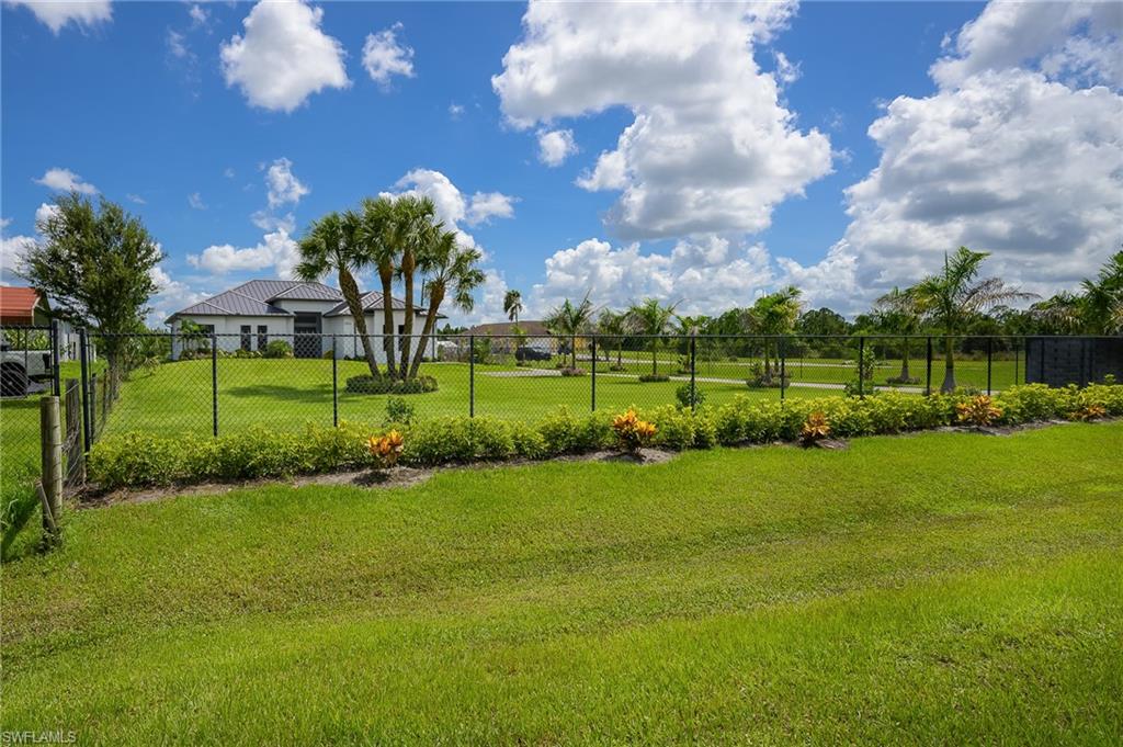 Expansive green lawn with a black chain-link fence, ornamental shrubs, and mature palm trees