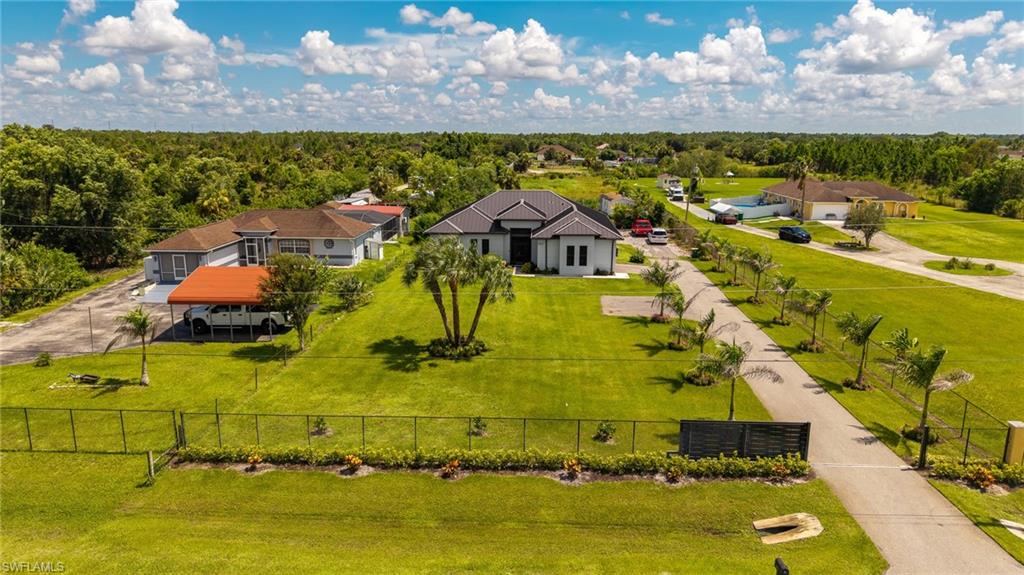Expansive property featuring a modern single-story residence with a dark roof and light exterior, a paved driveway lined with palm trees, and a substantial green lawn