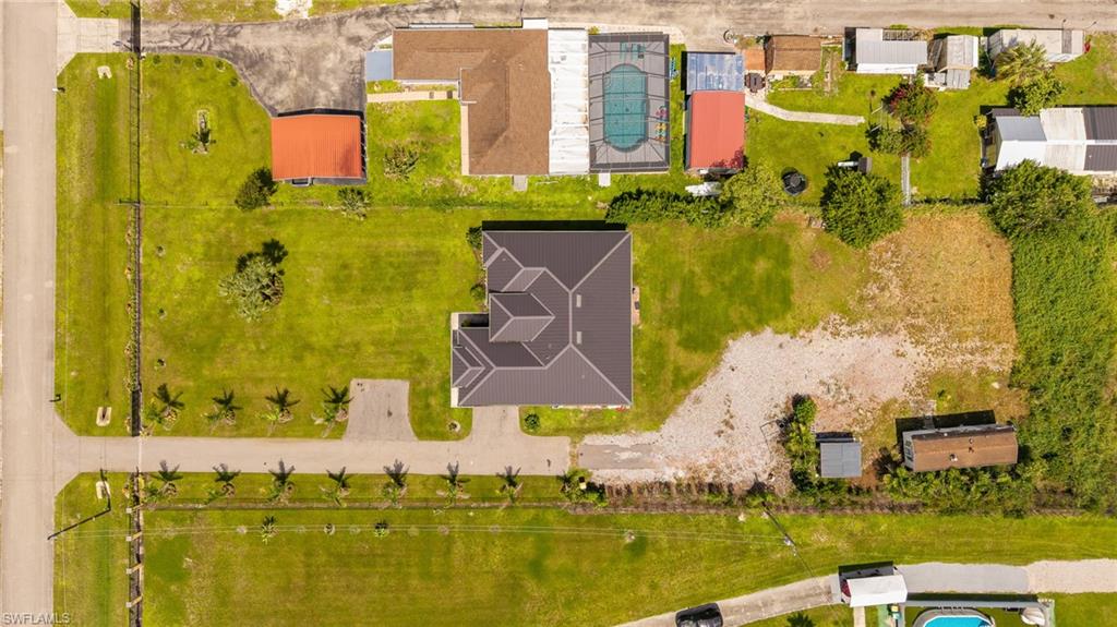 Expansive property featuring a dark-tiled roof structure, a paved driveway, a large grassy area, and mature palm trees lining the street
