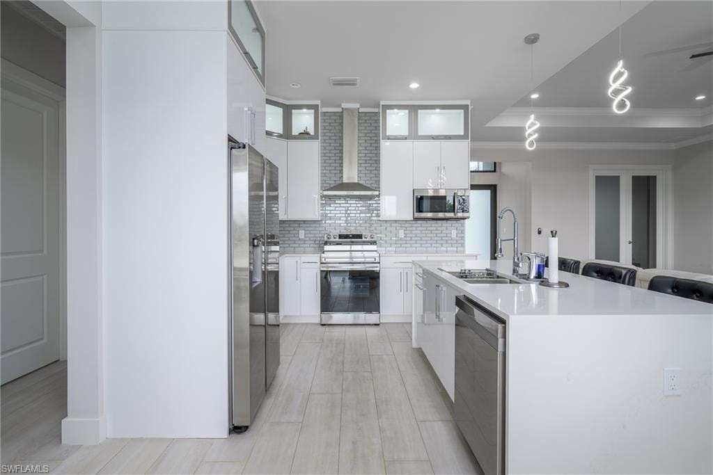Contemporary kitchen featuring a large waterfall-edge island with seating, stainless steel appliances, white cabinetry with glass accents, and a grey subway tile backsplash