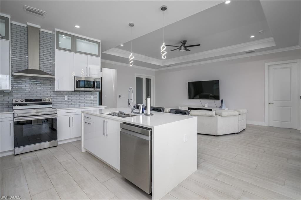 Modern kitchen featuring a large island, stainless steel appliances, gloss white cabinetry, and a subway tile backsplash