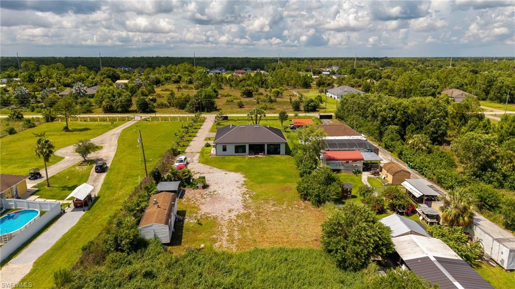 Expansive property featuring multiple structures, a main residence with a dark roof and light siding, an above-ground pool, and extensive green space