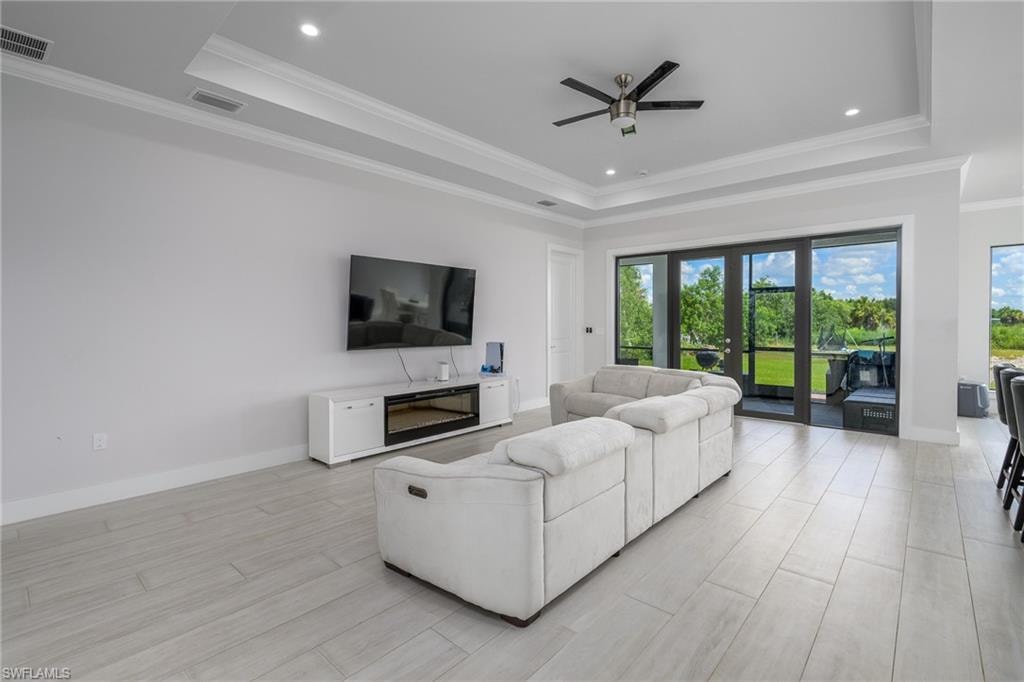 Spacious interior featuring light wood-finish flooring, a tray ceiling with recessed lighting and a ceiling fan, and large glass doors