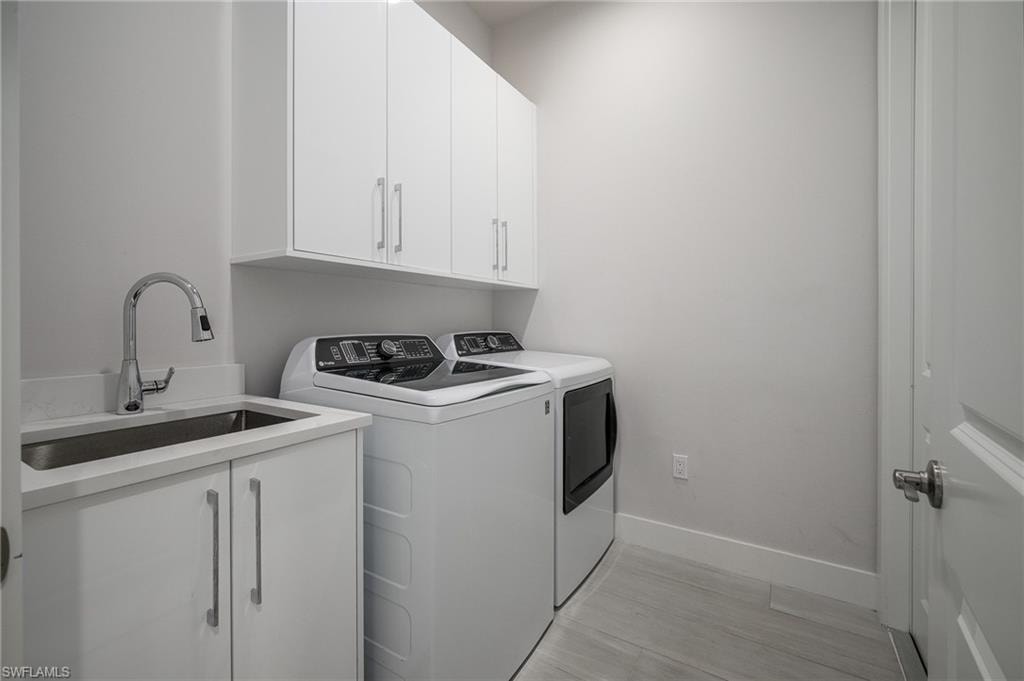 Laundry room featuring a utility sink with a high-arc faucet, white upper and lower cabinetry, light-toned flooring, and a white interior door with a silver handle