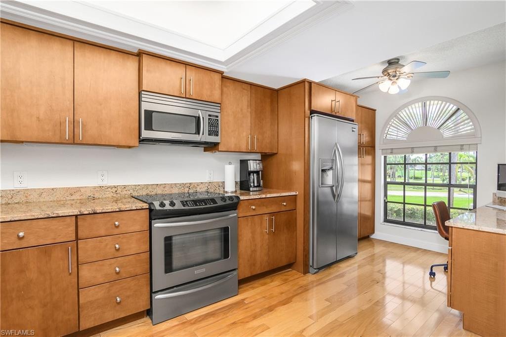 Kitchen with appliances with stainless steel finishes, brown cabinetry, light wood-style flooring, and ceiling fan and built in desk