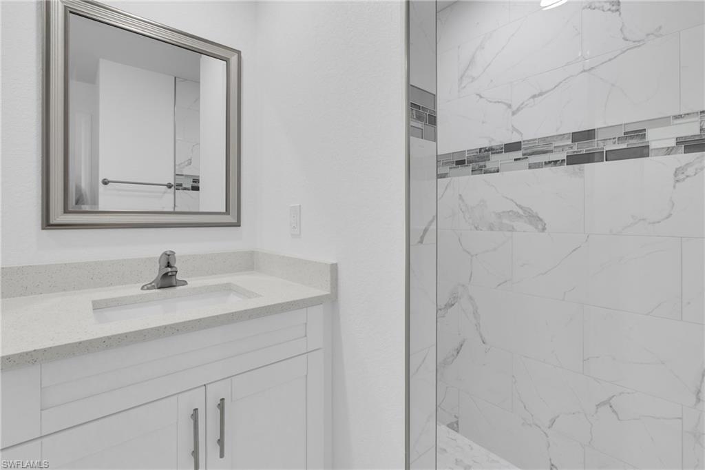 Bathroom vanity featuring a light-colored countertop with an integrated sink, white cabinetry with silver-toned hardware, and a framed mirror