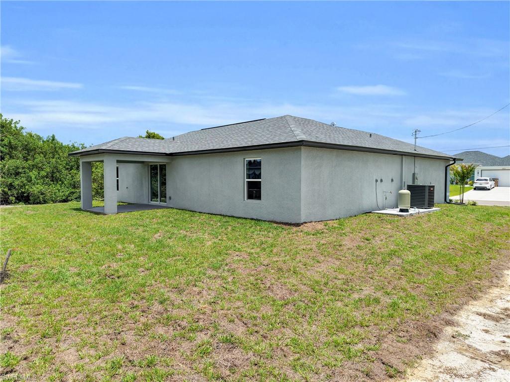 Exterior stucco finish with a shingle roof, featuring a covered patio with a concrete slab, sliding glass door access, and multiple windows