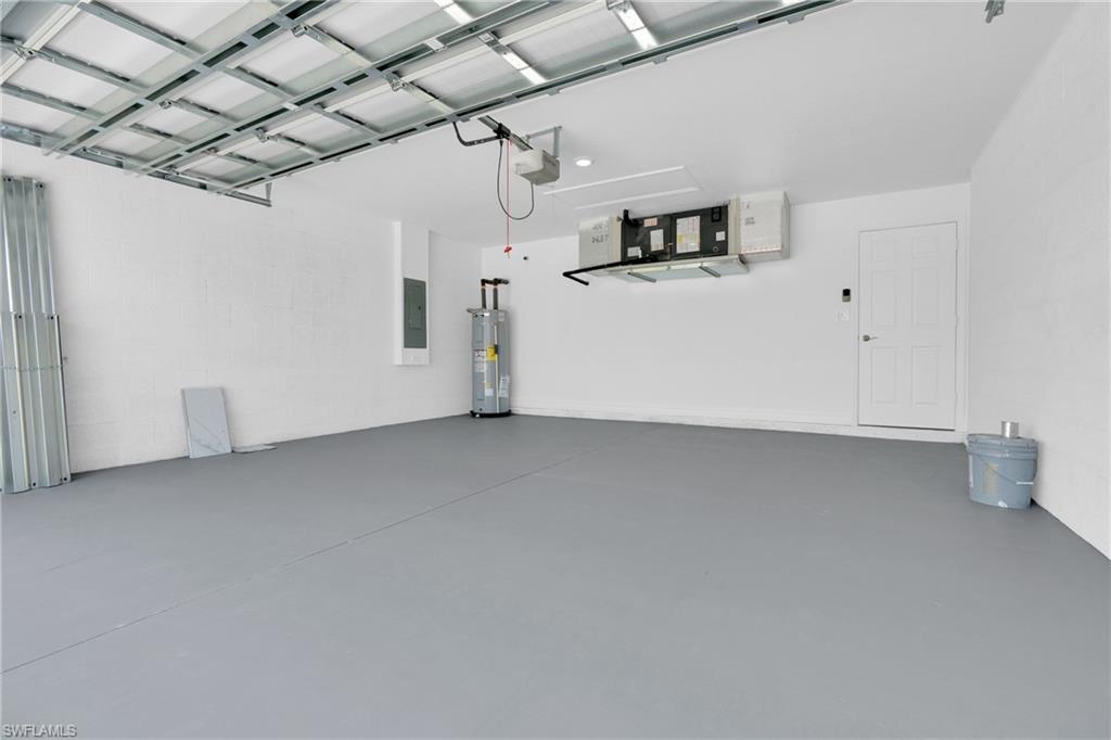 Spacious garage featuring a durable gray floor coating, white painted walls, exposed metal ceiling joists, an overhead garage door opener, and a side access door