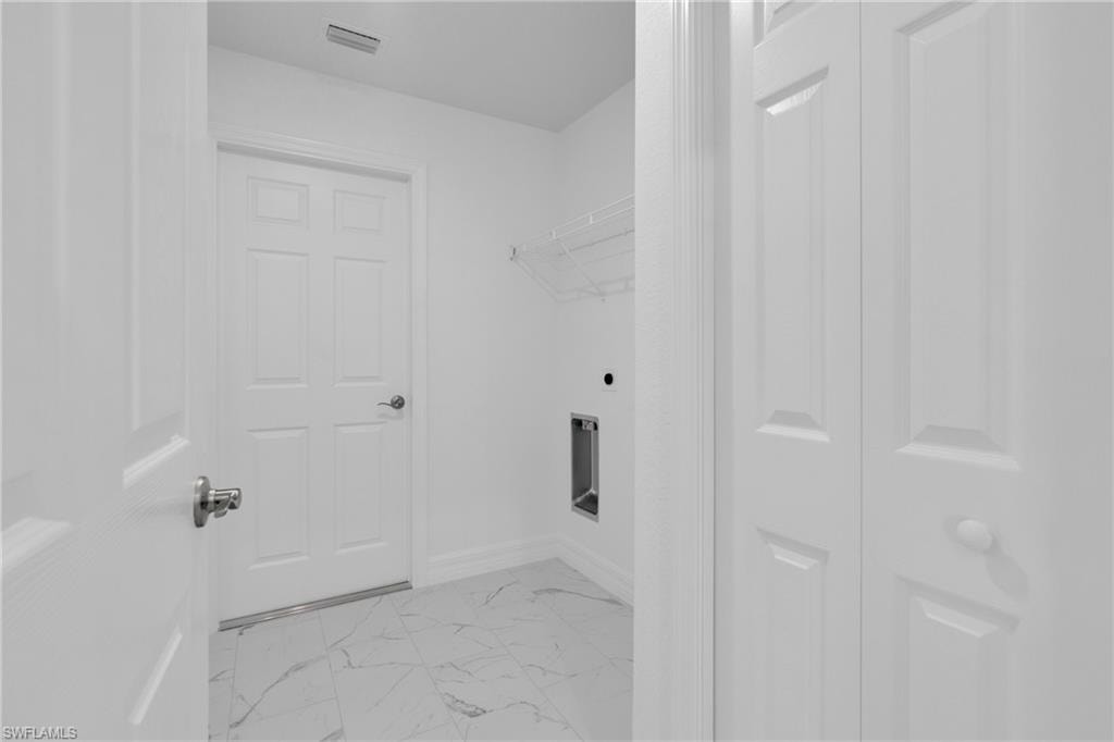 Utility room with white panel doors, white walls, and white veined tile flooring