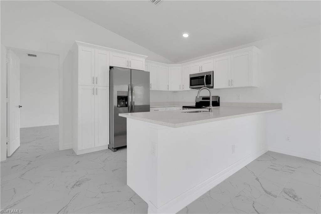 Modern kitchen featuring white shaker cabinetry, stainless steel appliances, a center island with sink, light-toned countertops, and marble-look tile flooring