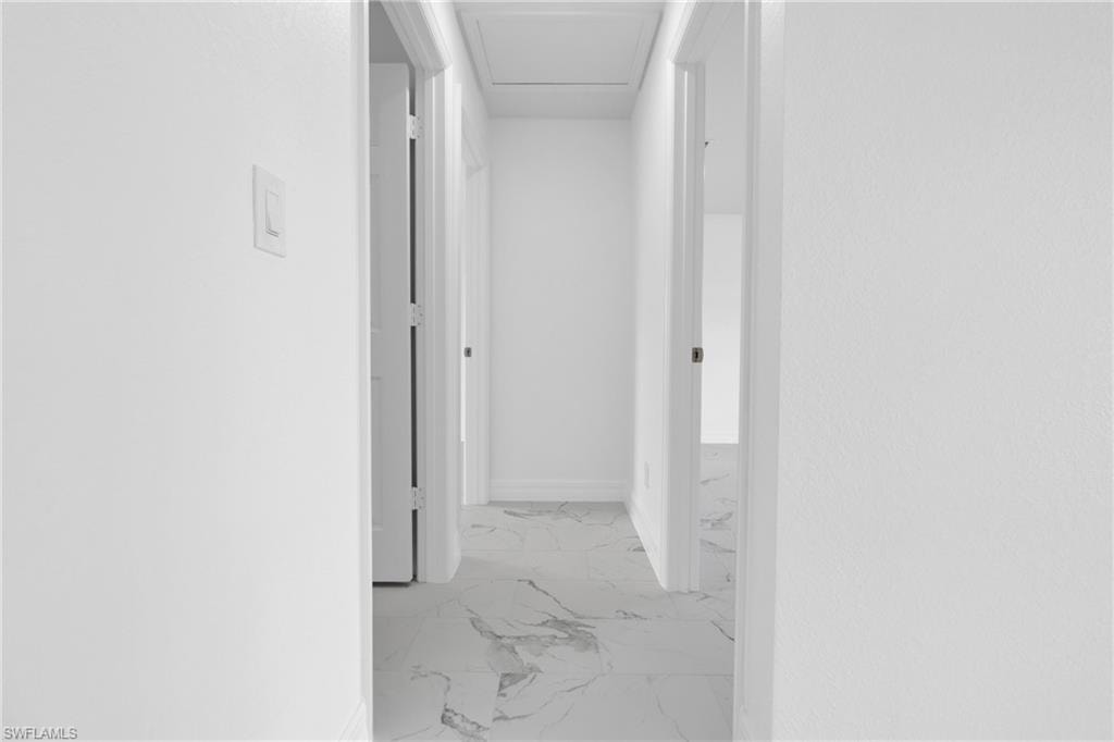 Hallway featuring white walls, white trim, white doors, and white marble-look tile flooring