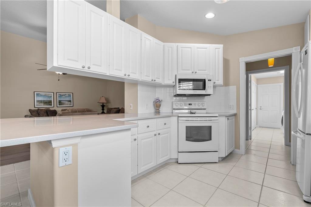Kitchen featuring white cabinetry, light-toned countertops, a white tile backsplash, an electric range, and tile flooring