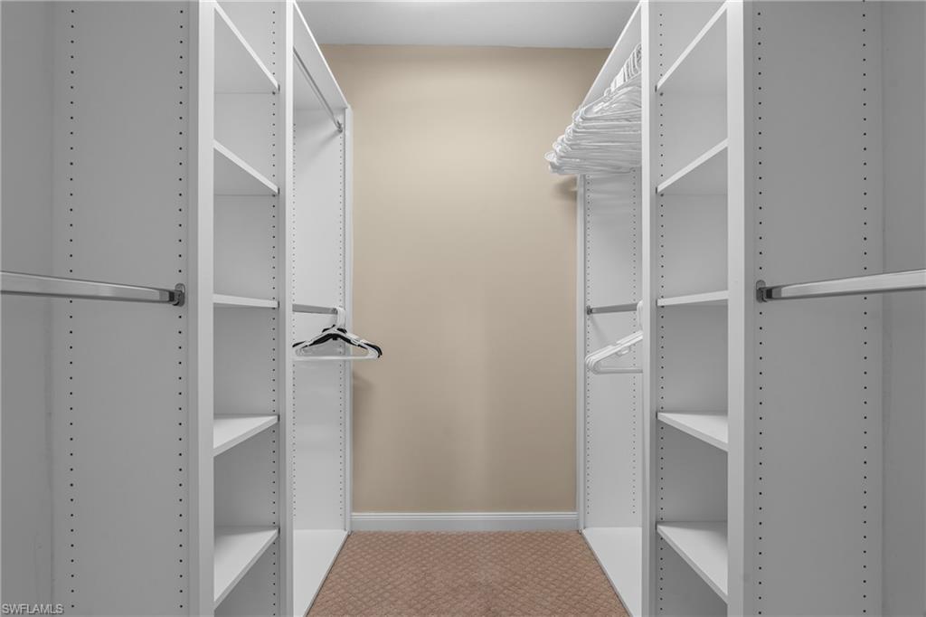 Walk-in closet featuring floor-to-ceiling white shelving units, multiple hanging rods, and light beige carpeting