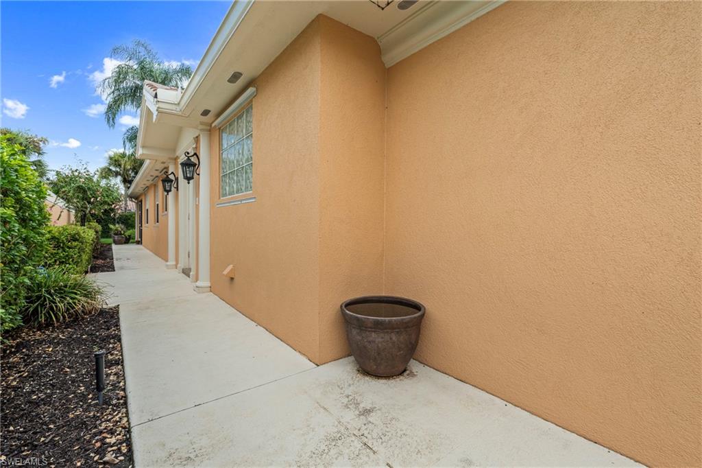 Stucco exterior with a concrete walkway, bordered by landscaped plantings and pathway lighting