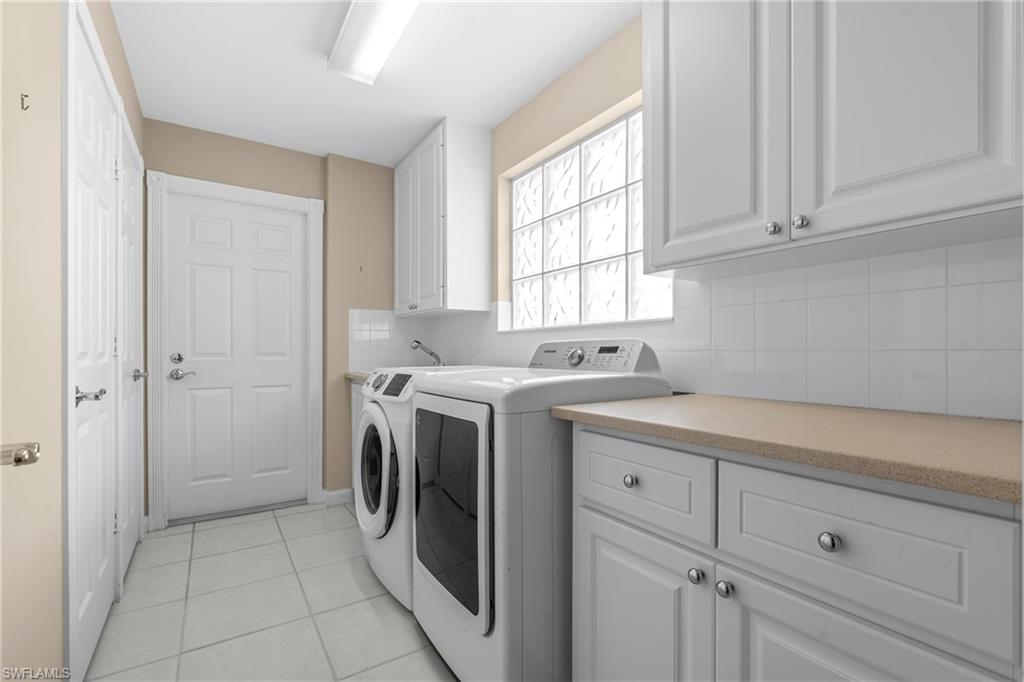 Dedicated laundry space featuring white cabinetry, a light-toned countertop, and a tiled backsplash