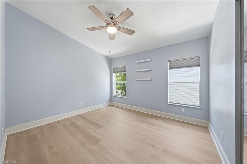 Room featuring wood-finish flooring, two windows with blinds, a ceiling fan with integrated lighting, and three wall-mounted shelves